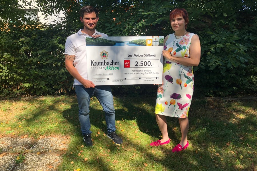 Simon Munaretto von der Krombacher Brauerei überreicht den Spendenscheck in Höhe von 2.500 Euro überreicht an die Lost Voices Stiftung
